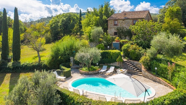 Une maison en pierre avec une piscine, entourée d’une végétation luxuriante et sous un ciel d’un bleu éclatant.