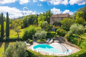 Une maison en pierre avec une piscine, entourée d’une végétation luxuriante et sous un ciel d’un bleu éclatant.