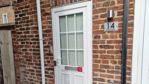 Eine weiße Tür mit Glasfenster, einem Schild mit der Nummer 14 und einem roten Lieferhinweisschild an der Wand.