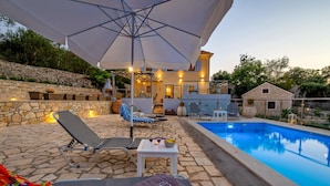 Zona de piscina con sillones de descanso, una mesa con bebidas y un muro de piedra.