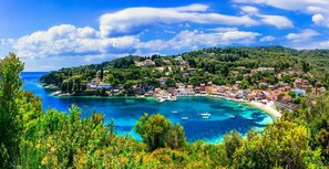 A coastal town with buildings along the shoreline, clear blue waters, and lush greenery.
