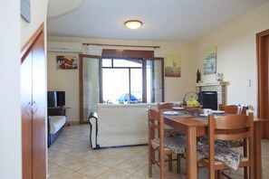 A dining area with a table set for four, a fireplace, and a window with curtains. - Villa Aetos Large Private Pool Sea Views A C Wifi Eco-friendly - 921 (Kefalonia)
