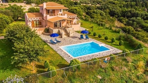 Ein zweistöckiges Haus mit Swimmingpool, umgeben von üppiger Vegetation und Hügeln.