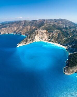 Eine Luftaufnahme einer Küstenlandschaft mit klarem, blauem Meer, einem Sandstrand und gebirgiger Landschaft.