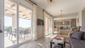 A spacious living room with a sofa, a coffee table, and a TV. There is a sliding glass door leading to a balcony with outdoor furniture. - Vatsa Beach Villa Large Private Pool Walk to Beach Sea Views A C Wifi - 3021 (Kefalonia)