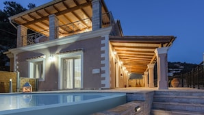 Eine zweistöckige Villa mit Swimmingpool, einer überdachten Terrasse und Blick auf die umliegende Landschaft.