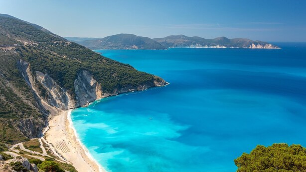 Eine Küstenlandschaft mit Strand, klarem blauen Wasser und gebirgiger Landschaft.
