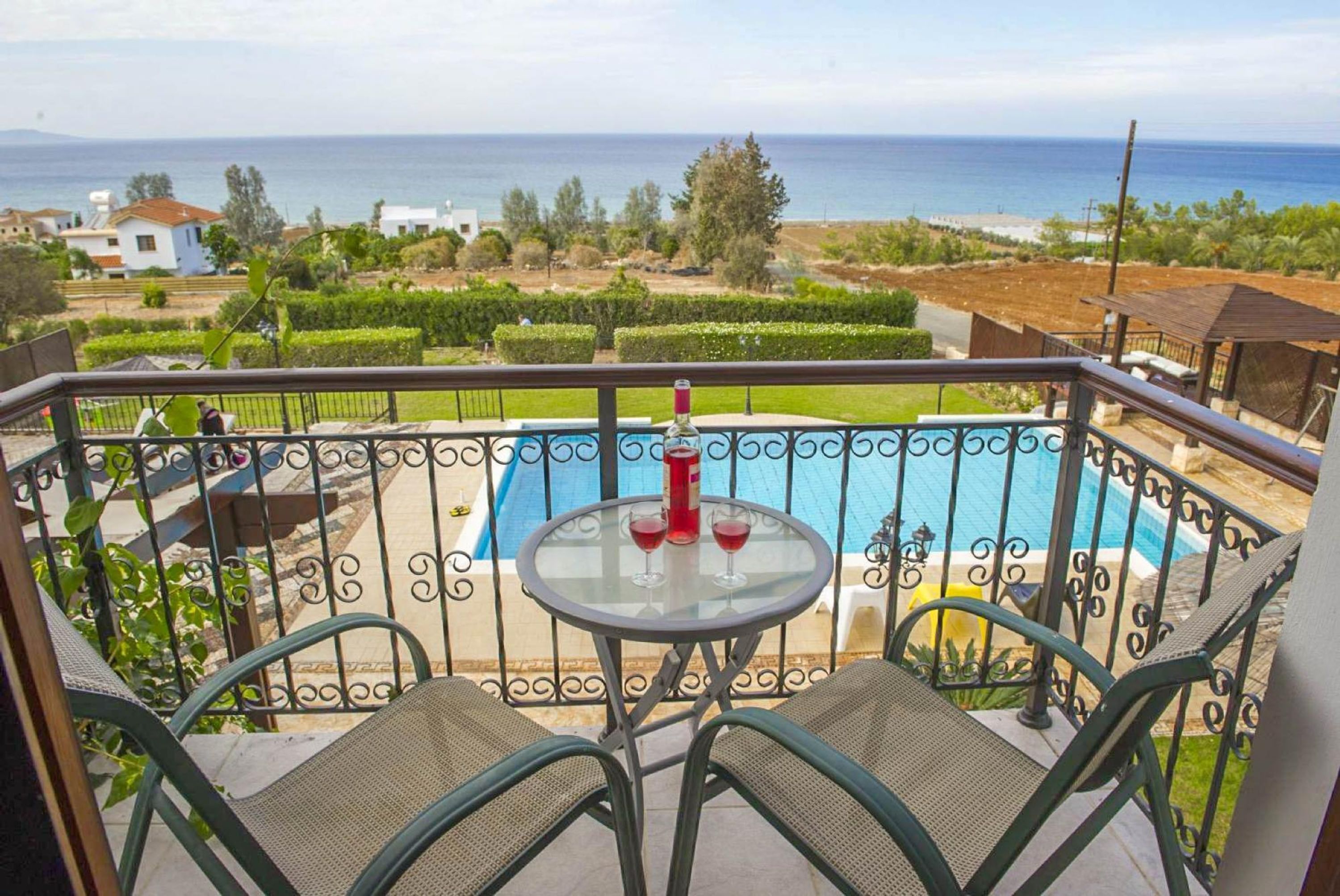 A balcony with a pool, two chairs, and a table with a bottle and glasses.