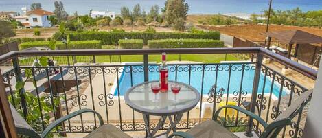 A balcony with a pool, two chairs, and a table with a bottle and glasses.