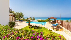 A backyard with a swimming pool, lounge chairs, a wooden deck, and a view of the sea. - Villa Minoas Large Private Pool Walk to Beach Sea Views A C Wifi Eco-friendly - 2565 (Argaka)