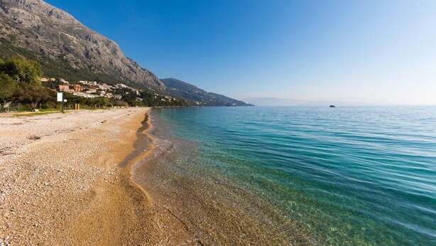 A pebble beach with clear water and a mountain backdrop. - Anna Apartment Walk to Beach A C Wifi Car Not Required - 2451 (Corfu)