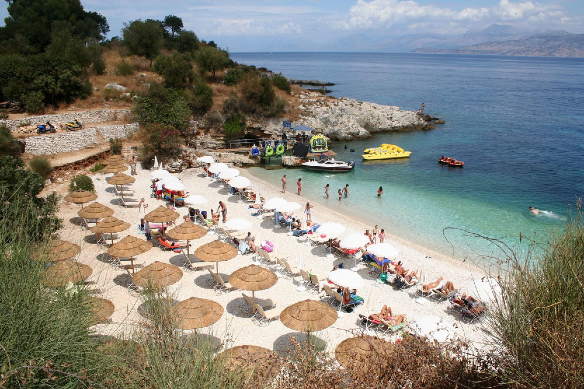 Ein Strand mit Liegestühlen und Sonnenschirmen, Booten und einer felsigen Küstenlinie.