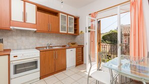 A kitchen with wooden cabinets, a white stove, and a glass table with chairs. - Anna Apartment Walk to Beach A C Wifi Car Not Required - 2451 (Corfu)