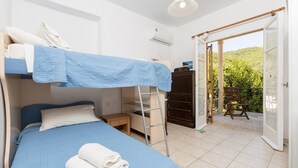 A compact room with bunk beds, a small desk, and a wardrobe. There is a balcony with a chair and a view of greenery. - Anna Apartment Walk to Beach A C Wifi Car Not Required - 2451 (Corfu)