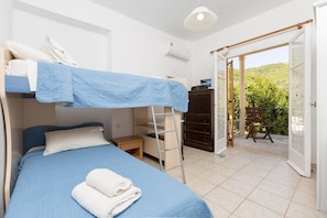 A compact room with bunk beds, a small desk, and a wardrobe. There is a balcony with a chair and a view of greenery.