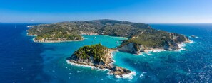 Vista aérea de una zona costera con aguas turquesas cristalinas, afloramientos rocosos y una pequeña isla con vegetación densa.