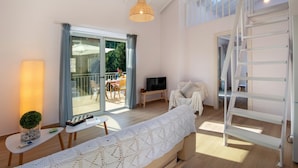 A spacious living room with a large window, a cozy sofa, a TV, and a ladder leading to an upper level. - Villa Ifigeneia Swimming Pool Walk to Beach Sea Views A C Wifi - 3455 (Paxos)