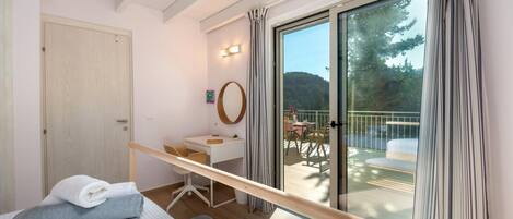 Ein Schlafzimmer mit Bett, Schreibtisch, Stuhl, Fenster und einem Balkon mit Tisch und Stühlen.