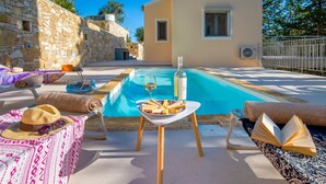 A poolside area with a stone wall, a pool, lounge chairs, a table with food and drinks, and a building in the background. - Villa Alexandros Swimming Pool Walk to Beach A C Wifi - 3454 (Paxos)
