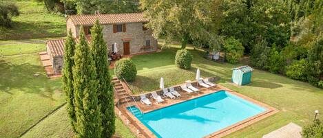 A swimming pool with lounge chairs, a stone building, and surrounding greenery.