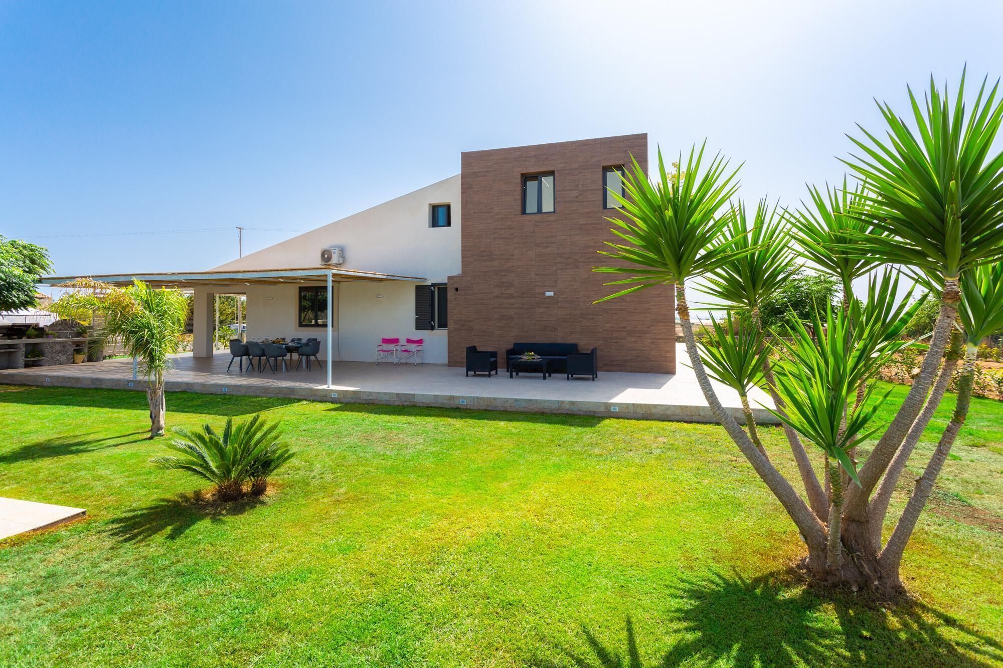 A modern house with a covered patio, outdoor seating, and a well-maintained lawn.