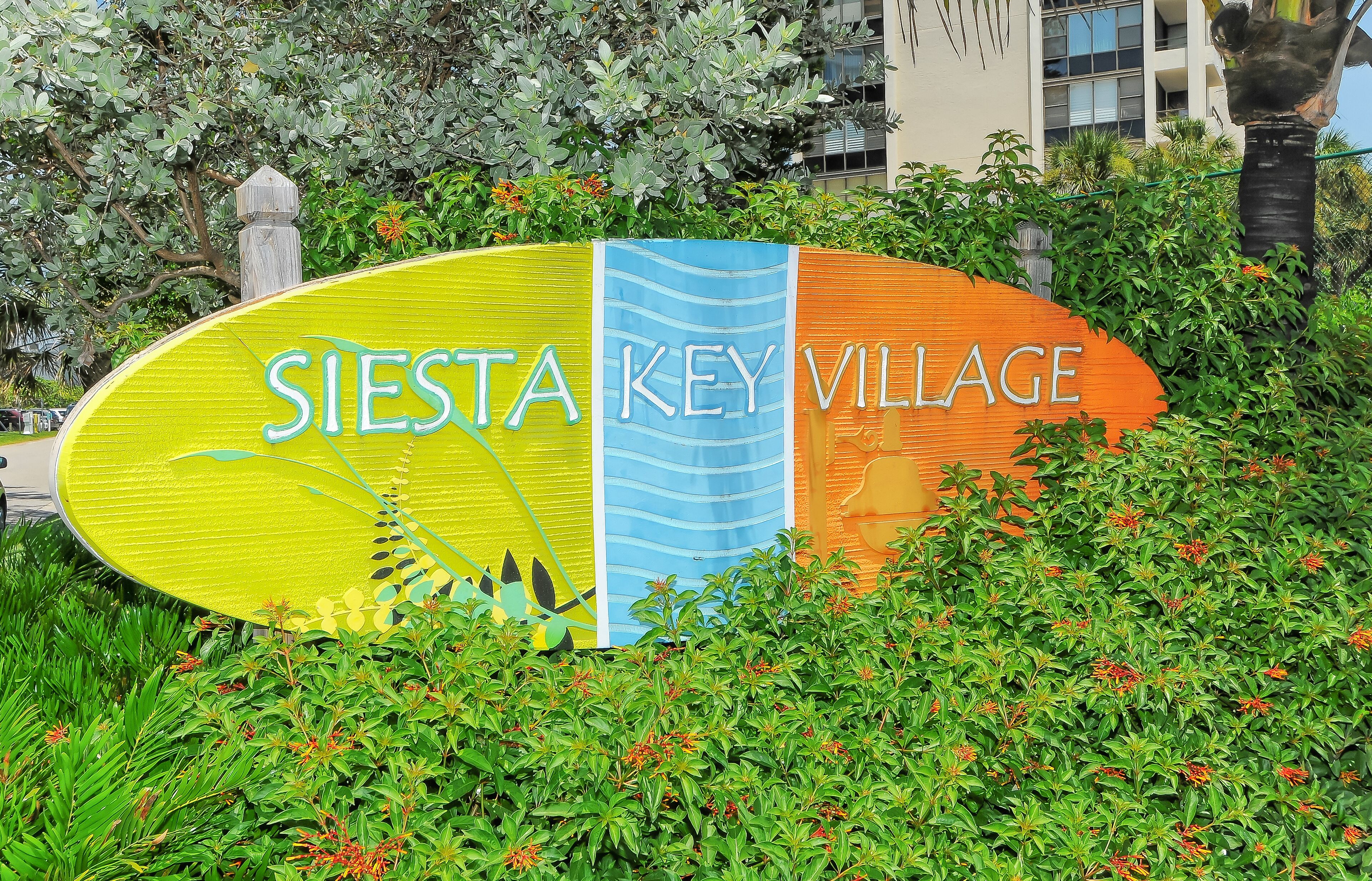 Une enseigne pour le village de Siesta Key, avec un design coloré et des plantes vertes tout autour.