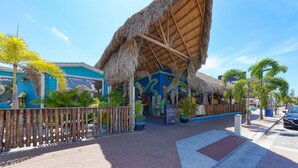 A tropical-themed restaurant with a thatched roof, bamboo fence, and colorful murals.