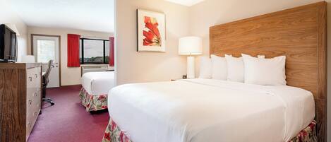 A hotel room with a large bed, a desk with a chair, a TV, and a window with red curtains.