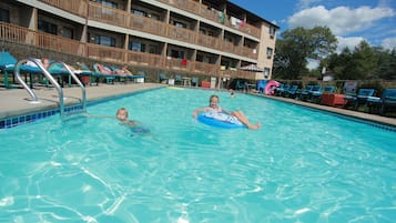 Una piscina con sillones de descanso y un edificio de varios pisos al fondo.