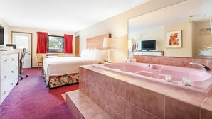 Hotelkamer met een groot bed, een apart bureau met stoel, een grote spiegel, een televisie en een ruim bad.