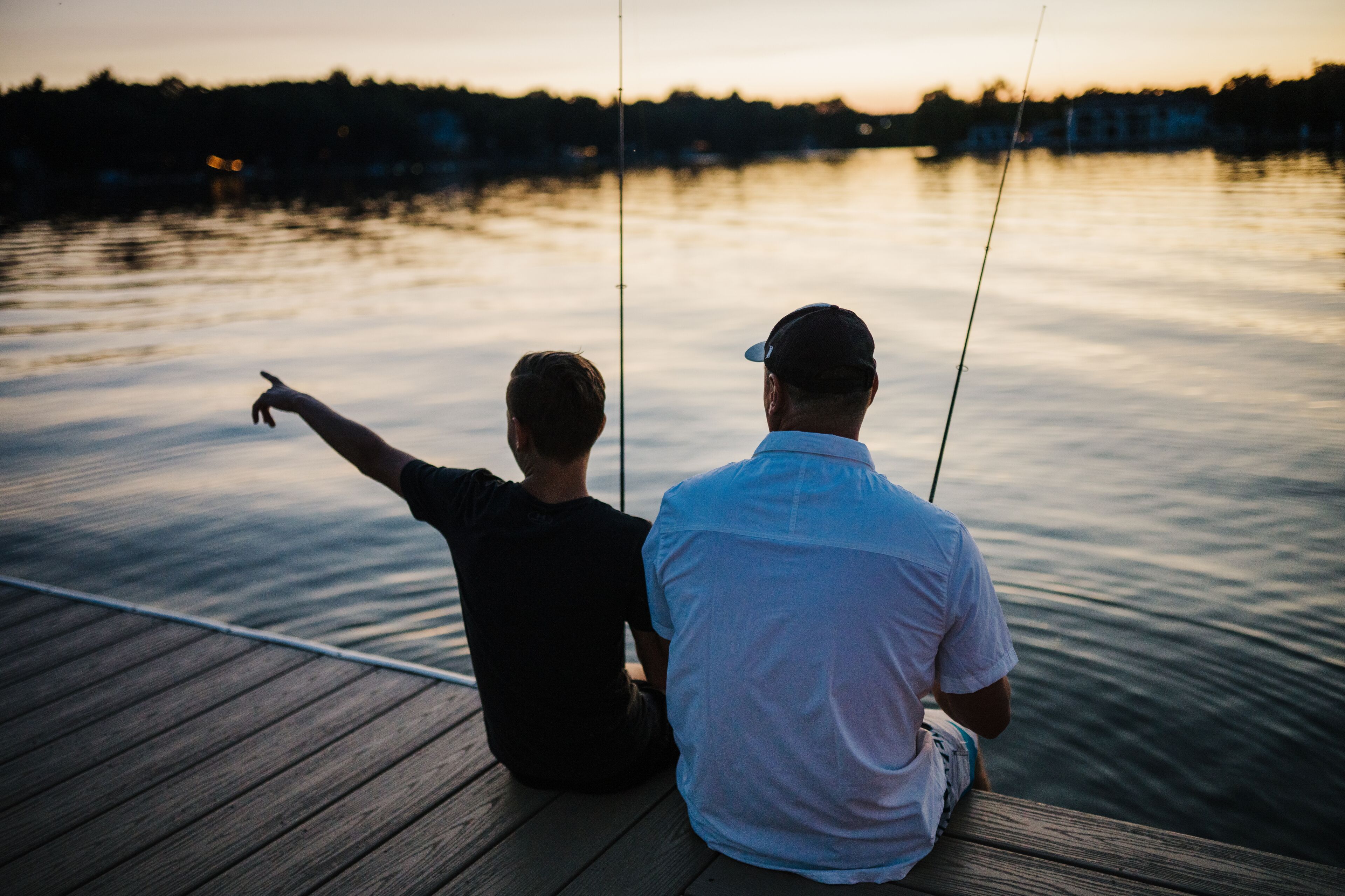 Two people sitting on a wooden dock, fishing.