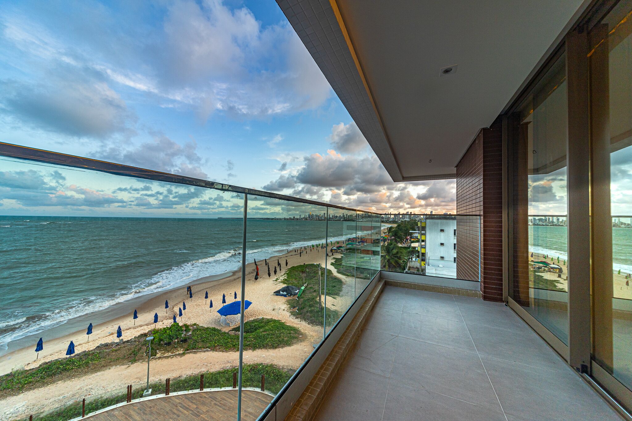 A balcony with a glass railing overlooking a beach and ocean.