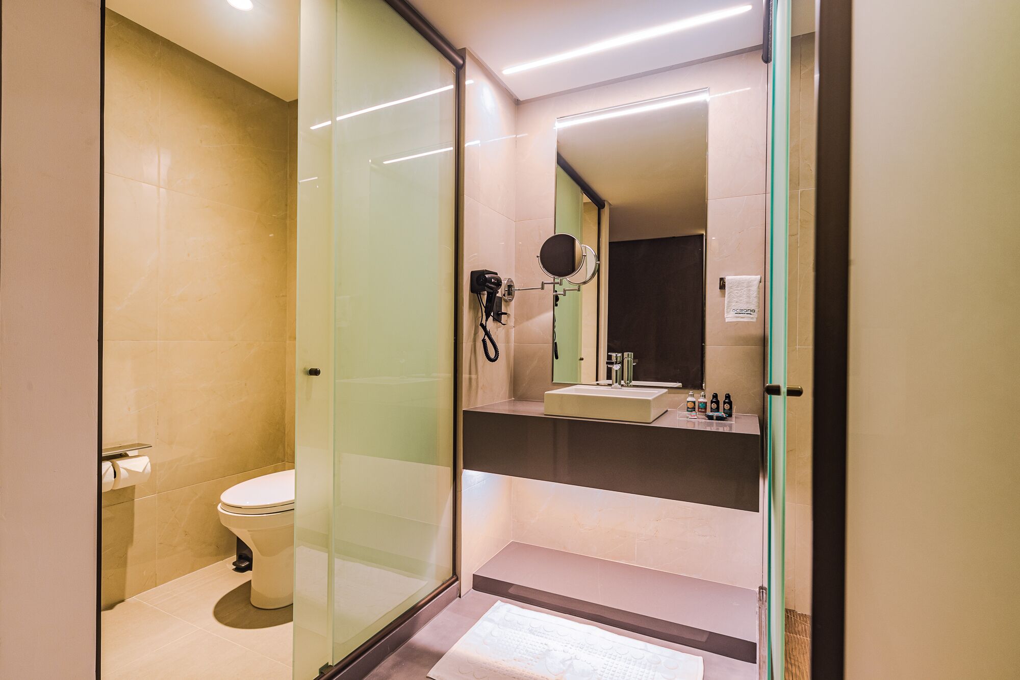 Un baño moderno con cabina de ducha de vidrio, inodoro, lavabo con espejo y secador de pelo.