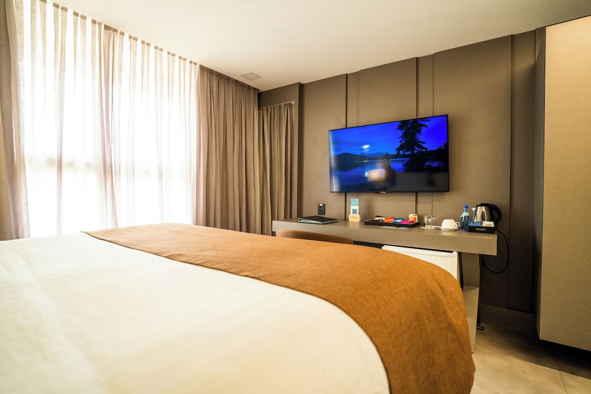 Une chambre d’hôtel avec un grand lit, un bureau doté d’un téléviseur à écran plat, une machine à café et une vue sur l’extérieur par la fenêtre.
