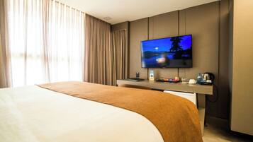 A hotel room with a large bed, a desk with a flat-screen TV, a coffee maker, and a view of the outdoors through the window.