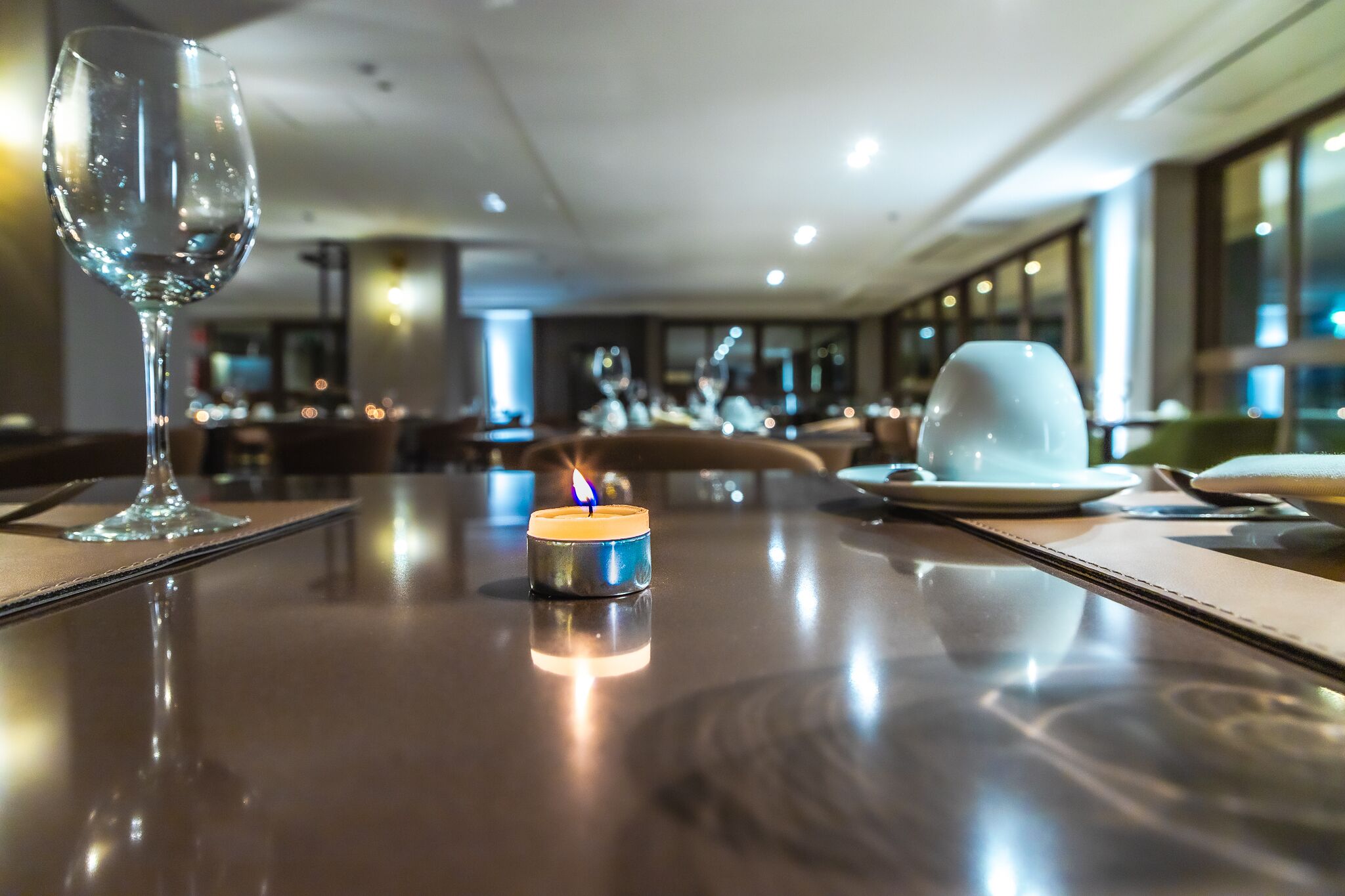 A dining table with a candle, a wine glass, and plates in a modern restaurant setting.