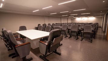 A conference room with a long table and rows of chairs, equipped with overhead lighting.