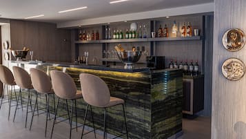 A modern bar area with a marble countertop, bar stools, and a variety of liquor bottles.
