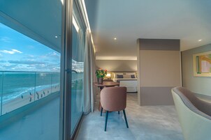 Un balcone con vista sulla spiaggia e sull'oceano, un'area salotto con tavolo e sedie, e un letto anch'esso con vista.