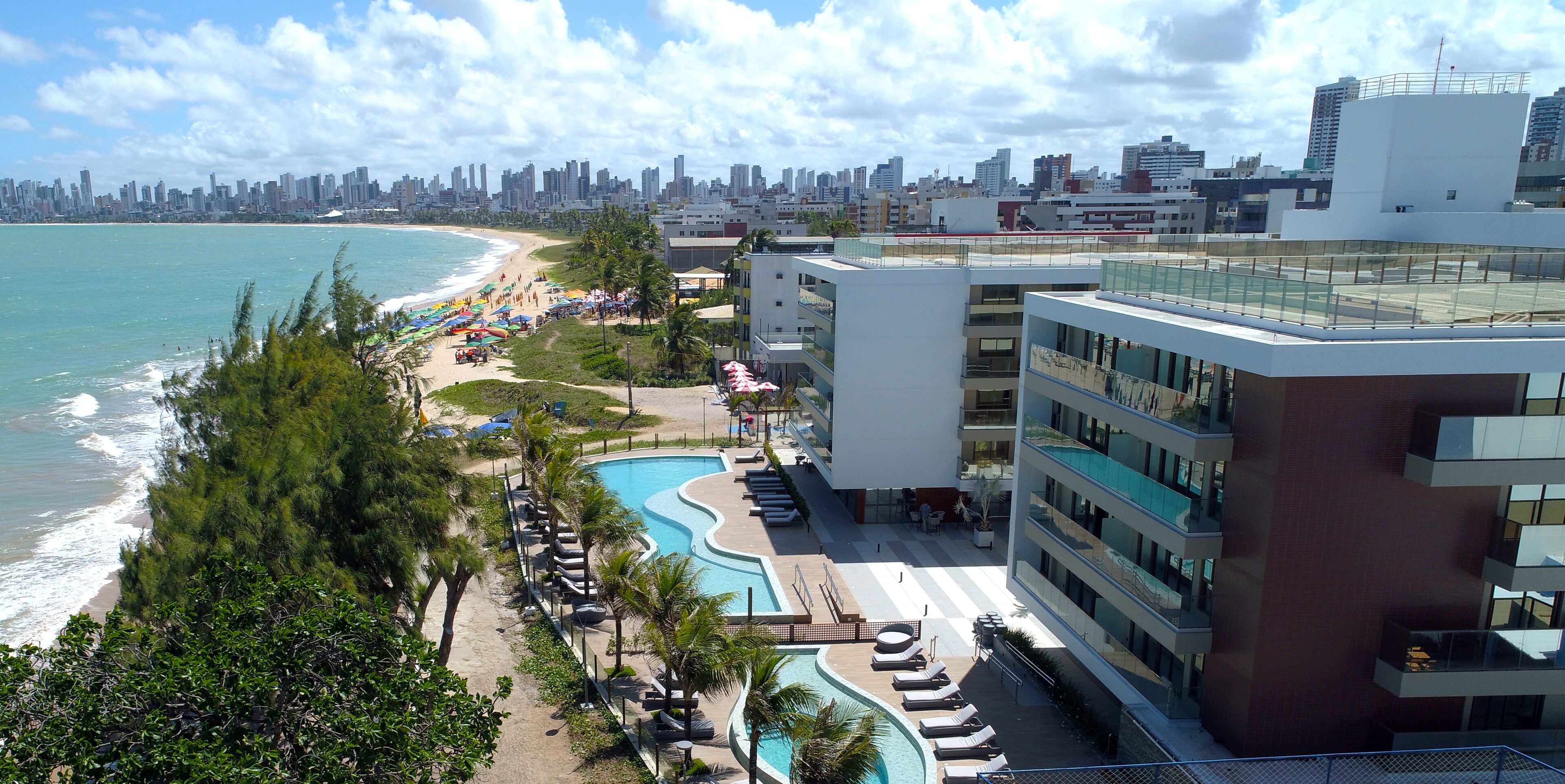 A resort with a swimming pool, beach, and city skyline in the background.