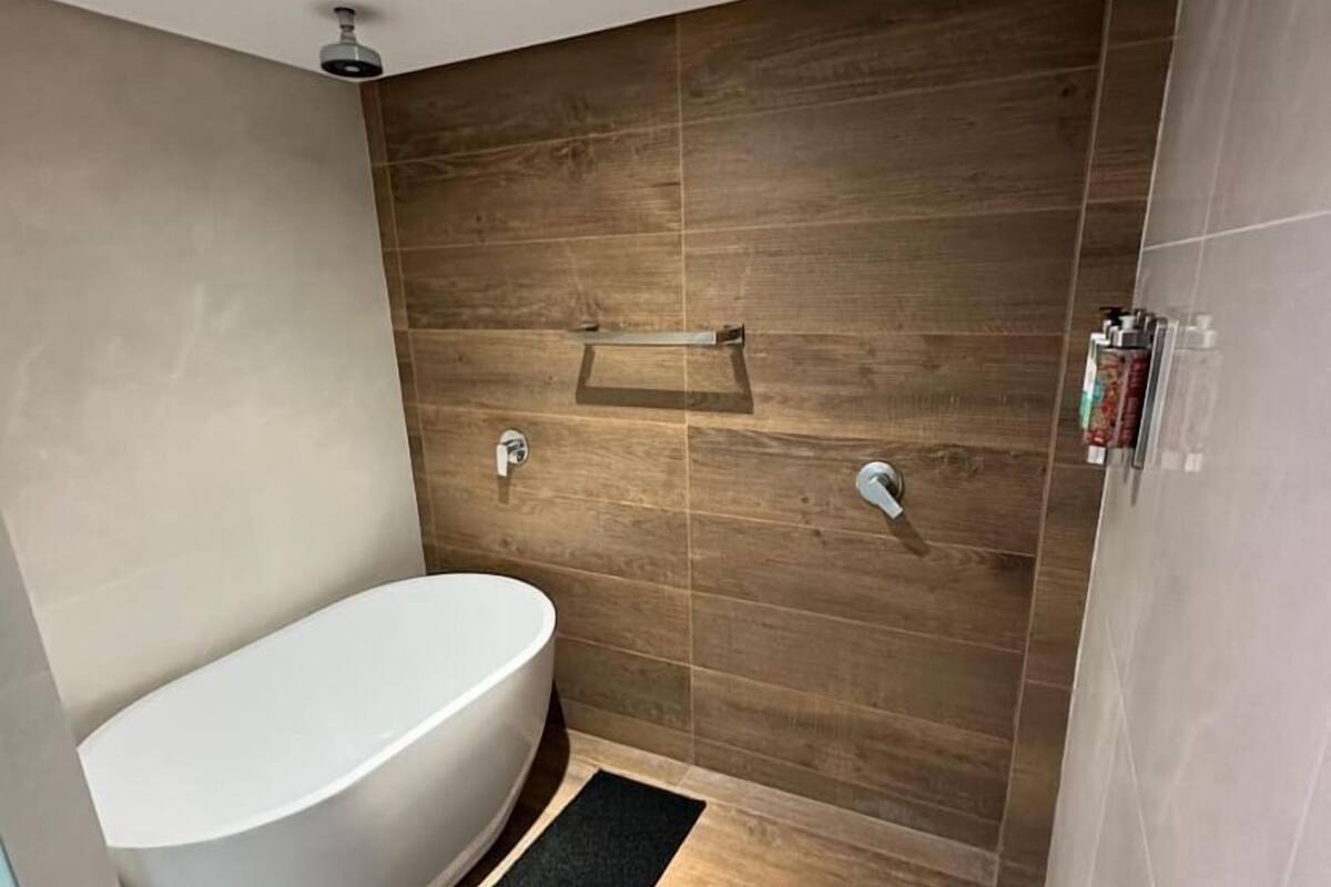 Une salle de bain moderne avec une baignoire sur pieds, des carreaux de mur en bois et un paillasson noir.