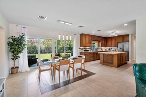 Una cocina moderna con armarios de madera, una isla central y un comedor con mesas y sillas de vidrio.