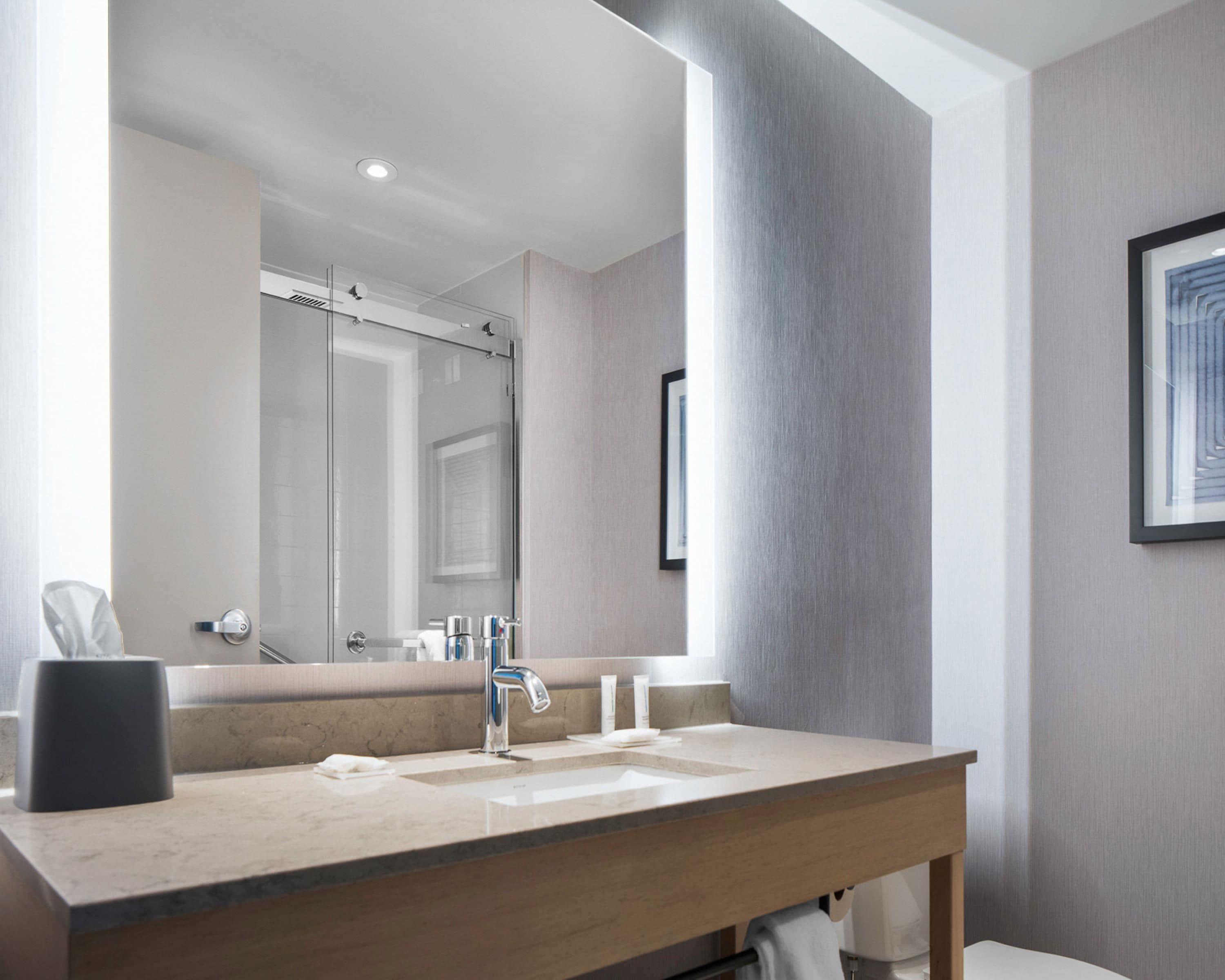 A modern bathroom with a large mirror, a sink, and a towel rack.