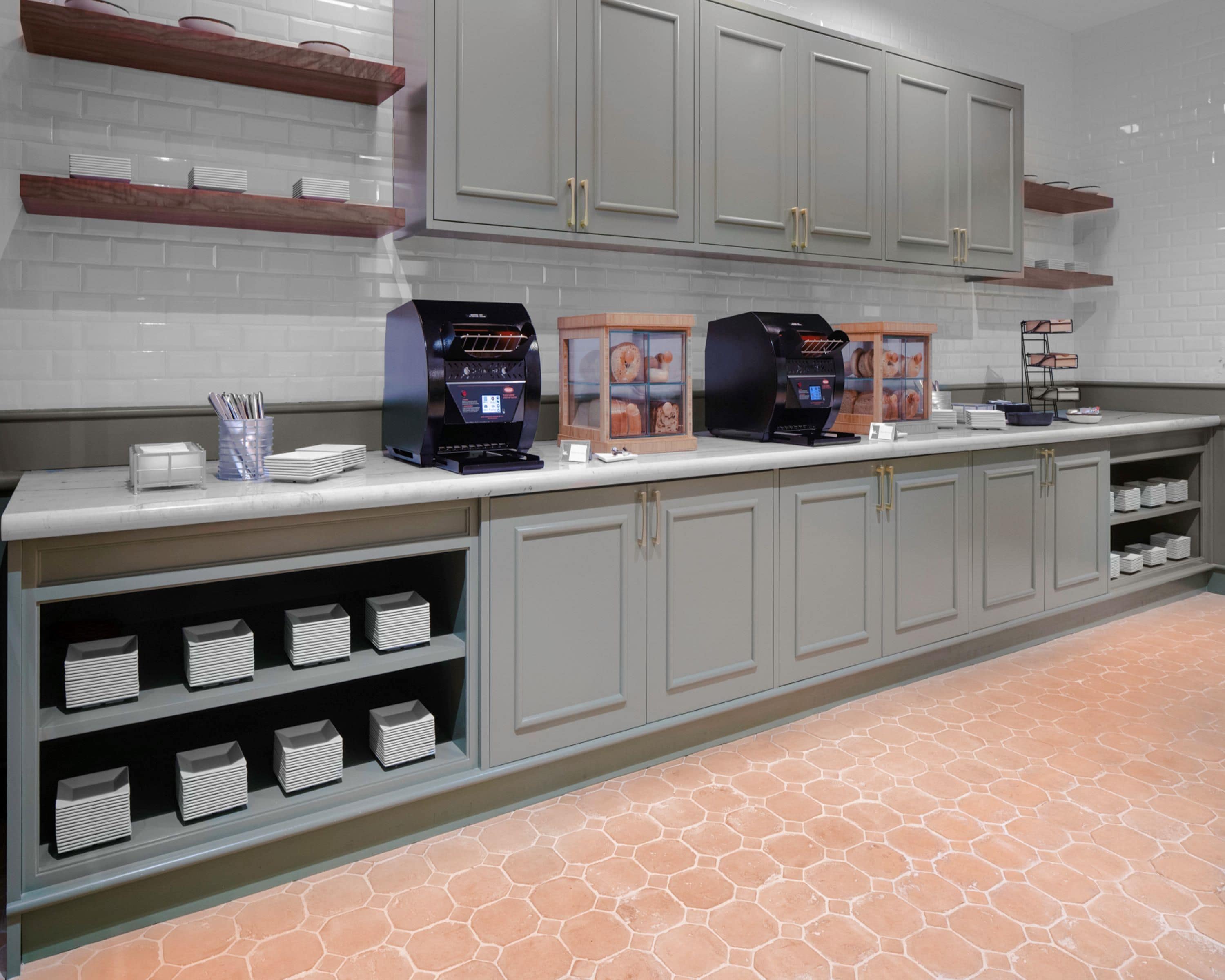 A commercial kitchen with two coffee machines, a display case with pastries, and neatly arranged white plates and bowls.