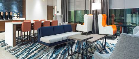 A modern hotel lobby with a sofa, chairs, a coffee station, and a large window with curtains.