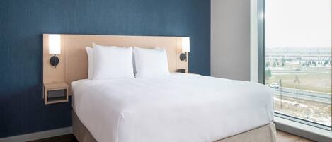 A modern hotel room with a large bed, two bedside tables, and a view of a cityscape through a large window.
