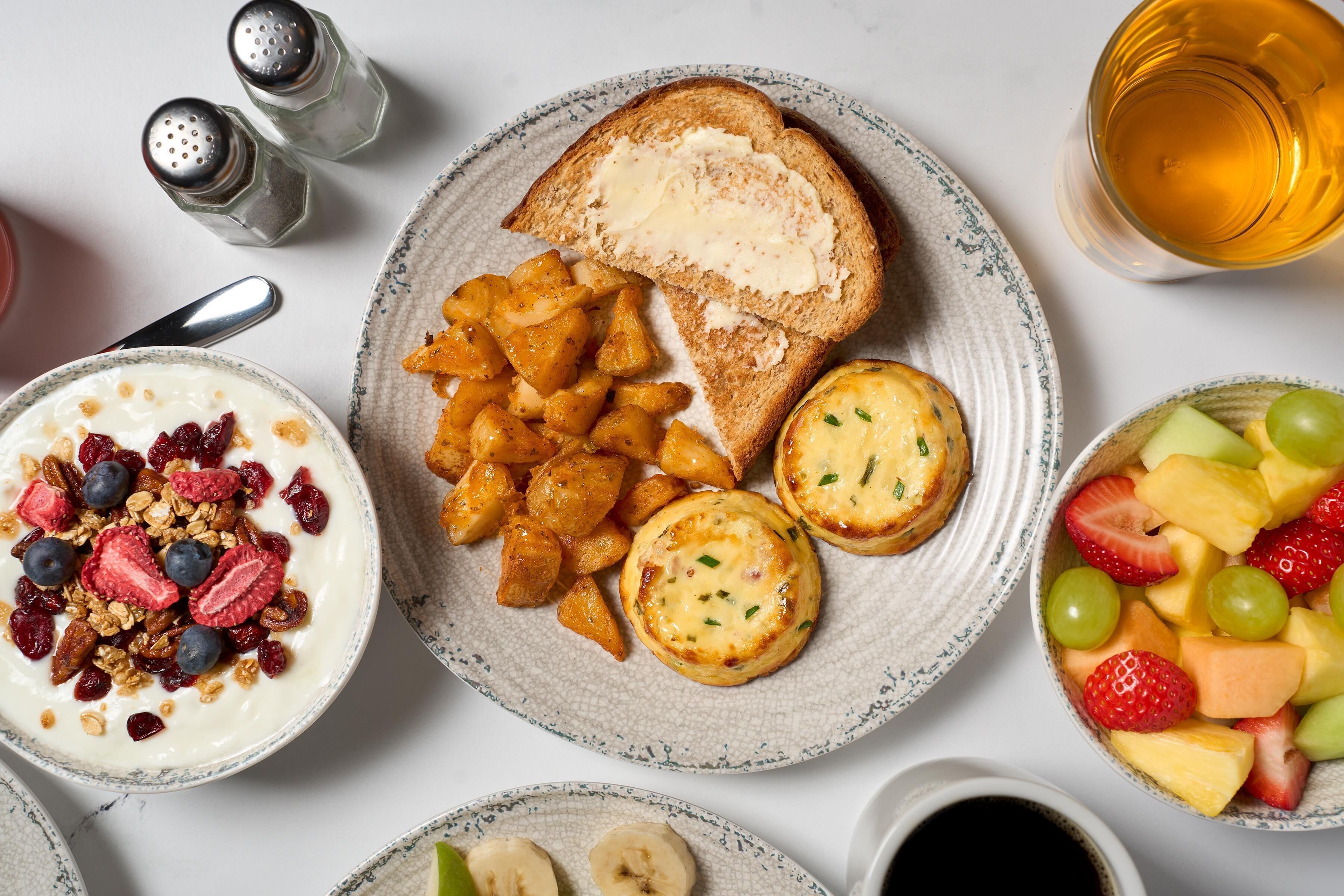 Uma mesa de café da manhã com torradas, frutas, iogurte e uma xícara de chá.