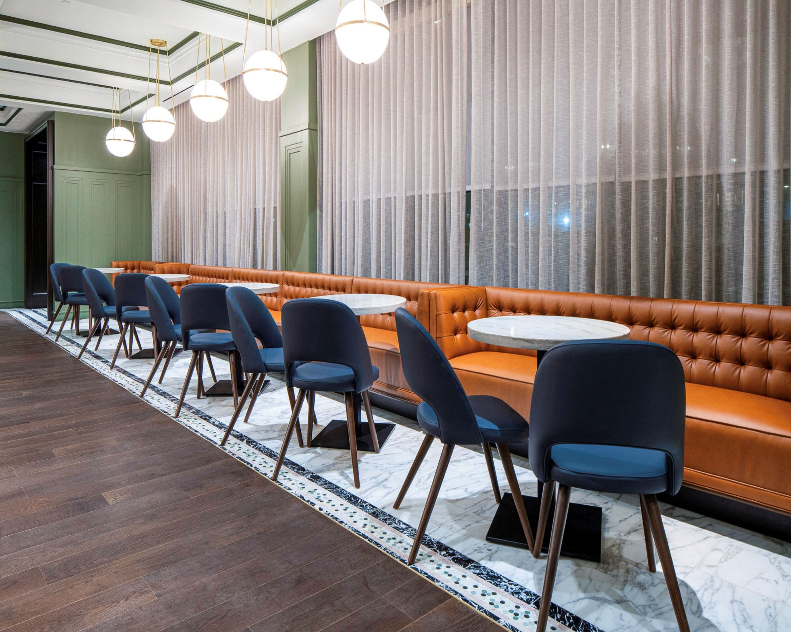 A restaurant with a long counter, blue chairs, and a brown leather booth.