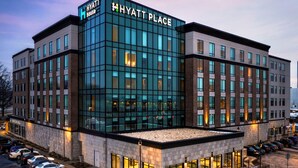Een modern Hyatt Place hotel met een glazen gevel, meerdere parkeerplaatsen en een goed verlichte buitenkant.