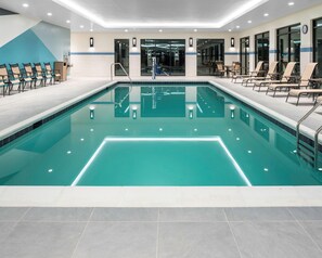 Una piscina con solárium azulejado, sillas de descanso y zona de vestuarios.